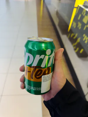 Zielono-żółta puszka trzymana w jasnym wnętrzu przy schodach ruchomych.