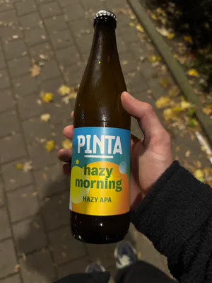 Ciemna szklana butelka z turkusową etykietą nad chodnikiem pokrytym liśćmi.